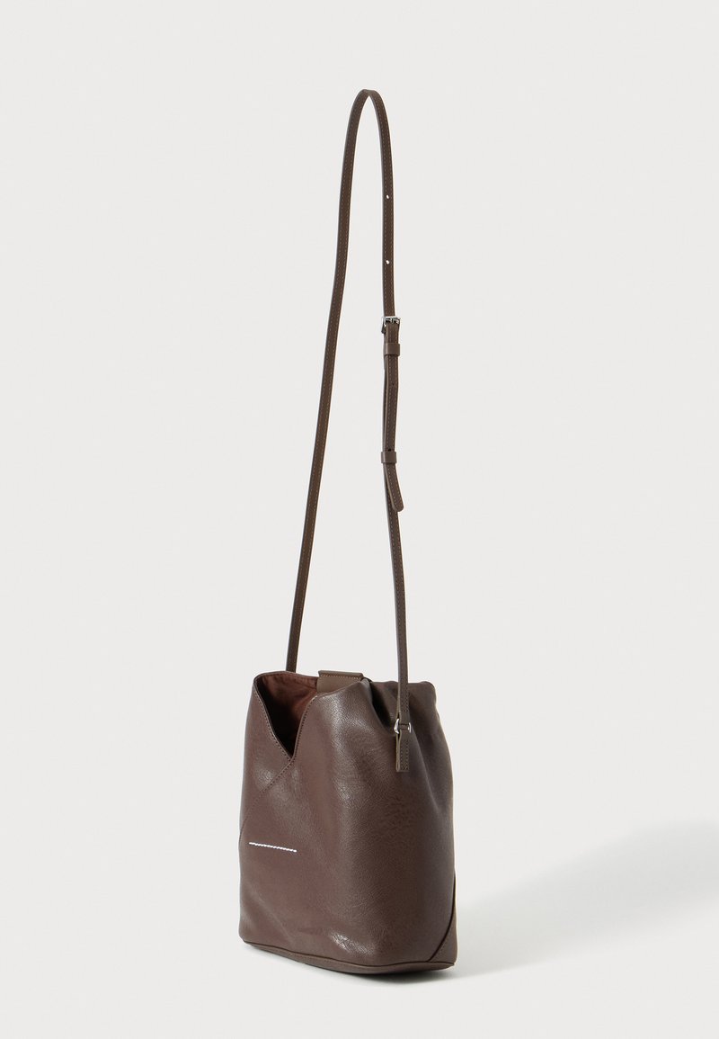 Sac seau en cuir marron avec bandoulière longue réglable et détail discret de couture horizontale sur fond clair uni.
