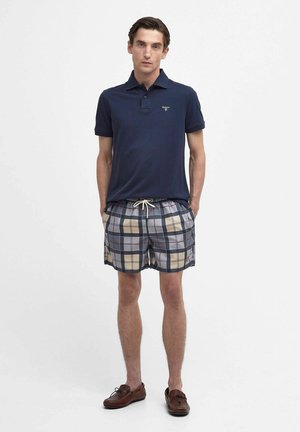 Navy polo shirt with short sleeves, paired with beige and navy plaid swim shorts with drawstring. Brown boat shoes complete the look.
