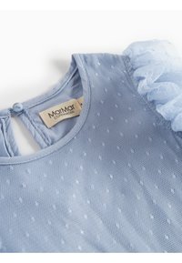 Blouse bleu clair avec un tissu texturé aux motifs à pois subtils, accents en tulle froncé sur une épaule et fermeture à boutons au dos.