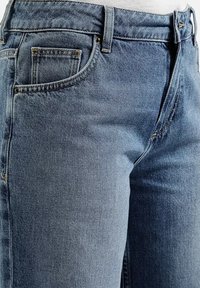 Zbliżenie na jasnoniebieskie dżinsy na talii i górnej części uda, ukazujące przednie kieszenie, szlufki na pasek i metalowe nitki.