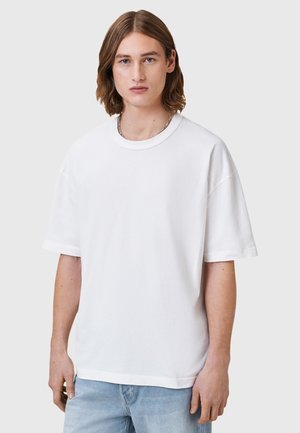 T-shirt bianco in cotone, colletto tondo, maniche corte, vestibilità comoda, texture liscia, abbinato a jeans di denim blu chiaro. Senza motivi o dettagli.