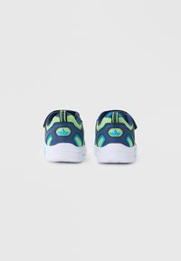 Zadní pohled na tmavě modré a zelené sportovní boty s bílou podešví, vybavené suchým zipem, texturovanými akcenty a kontrastními detaily na patě.