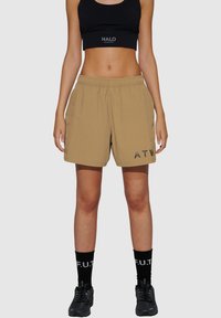 Tan sportieve shorts met een elastische tailleband, zijzakken en zwarte 'ATW'-tekst op het linkerpantalon. Draagt zwarte sokken en schoenen.