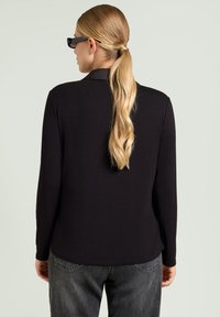 Top nero a maniche lunghe con colletto classico, realizzato in tessuto morbido. Indossato con jeans grigi scuri, dal taglio rilassato e con cuciture in vista.