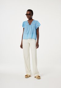 Blauw geborduurd topje met een gegolfde halslijn en korte fluttermouwen, gecombineerd met witte wijde broekspijpen en espadrille wedges.