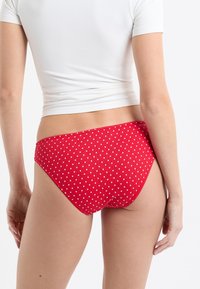 Roter Bikiniunterteil mit weißen Polka-Dots, mit geripptem Stoff und mittelhohem Bund. Glatte Kanten und eine figurbetonte Silhouette.