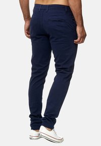 Pantalones entallados azul marino hechos de algodón, con una textura suave, bolsillos traseros y diseño de tiro bajo. Combinados con zapatillas blancas.