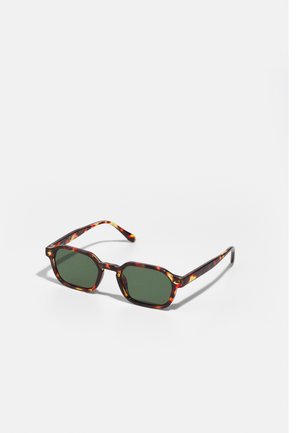 Óculos de sol em padrão tartaruga com lentes verdes, apresentando uma forma octogonal e hastes curvas e finas. O material tem um acabamento brilhante.