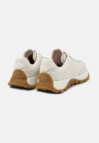 White leather sneakers with a cushioned sole, rubber outsole, and a textured brown heel. Features laces and subtle branding on the back.