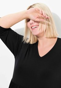 Mustat V-kaula-aukkoinen vaate, jossa on lyhyet hihat, rento malli ja sileä rakenne. Mallin hiukset ovat suorat ja hartiat pitkät.