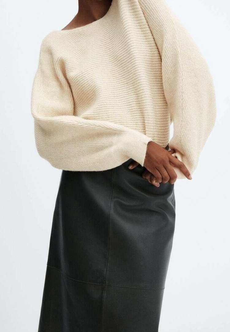 Pull en maille côtelée beige avec un design asymétrique, associé à une jupe en cuir noire présentant une texture lisse et des détails de couture.