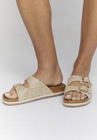 Beige gevlochten slidesandalen met twee verstelbare banden, kurken voering en een gestructureerde rubberen zool. Het open teen ontwerp zorgt voor ademend vermogen.