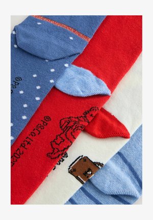 Four pairs of colorful socks: blue with polka dots and stripes, red with a graphic, cream with a bear, and light blue with stripes.