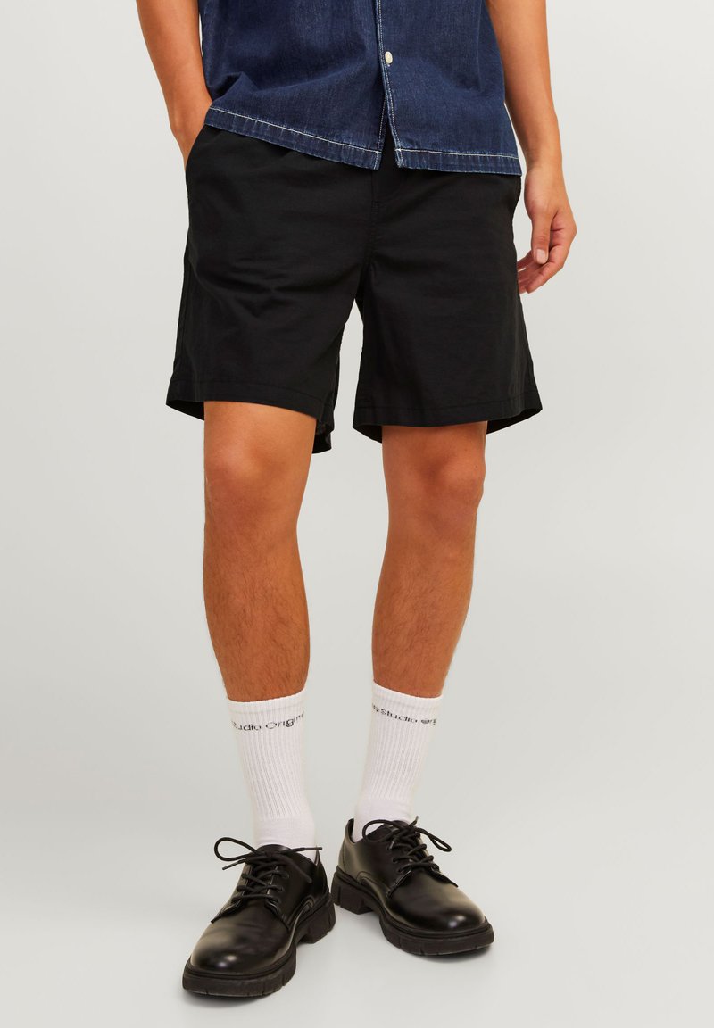 Black cotton shorts with a relaxed fit, paired with white socks and black lace-up shoes. Model wears a blue denim shirt.