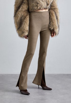 Pantalons taille haute à carreaux marron avec des ourlets évasés et fendus, associés à des talons aiguilles marron. Le tissu est texturé et ajusté.