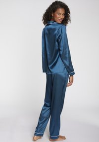 Satin-Pyjama-Set in Tiefblau. Langärmliges Hemd mit Kragen und weißen Pipings. Hose mit lockerer Passform und umgenähten Säumen. Glatte Textur.