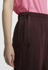 Maroon sweatpants with an elastic waistband and drawstring detail, paired with a loose-fitting pink top. Smooth fabric with a soft texture.