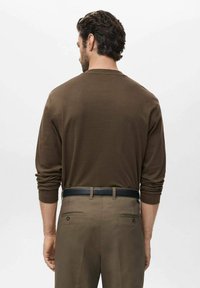 Smeđa košulja s dugim rukavima uparena sa svijetlosmeđim hlačama i crnim remenom. Košulja ima klasični okrugli izrez i kroj koji dobro pristaje.