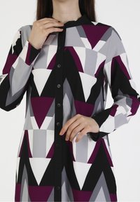 Robe à motifs abstraits avec des nuances de violet, gris, noir et blanc ; possède un devant boutonné et un col arrondi.