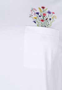 Bílý bavlněný tričko s květinovým designem v barvách jako je růžová, žlutá a fialová nad kapsou na hrudi. Měkká textilie, volný střih.