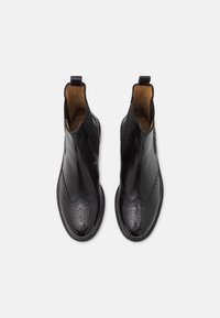 Bottines en cuir noir avec une finition lisse, détails brogue sur le bout, côtés élastiques et une languette à l'arrière pour un enfilage facile.