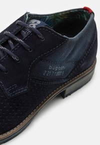 Scarpa elegante in suede blu scuro con dettagli perforati, pannello in denim a contrasto e fodera interna blu. Presenta una suola in gomma e un design con lacci.