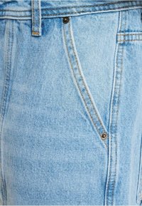 Tissu en denim bleu clair avec une poche avant, des rivets en laiton et des coutures orange sur un jean.