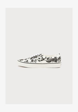 Baskets basses blanches Vans avec motif floral noir, lacets blancs et semelle en caoutchouc blanche avec bande noire.