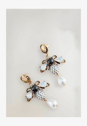 Kuldse tooniga kõrvarõngad, mis on kujundatud mesilaste sarnasteks, musta ja valge täpilise detailiga, kalliskivi kaunistustega ja tilgakujuliste pärlitega.