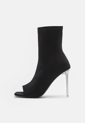 Sort ankelstøvle med åben tå og klar stiletthæl, glat stoføverdel, sidevisning på hvid baggrund.