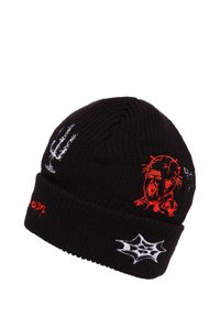 Cappello a maglia nero con design ricamati, tra cui un volto grafico rosso, ragnatela bianca e una silhouette di albero nera. Stile risvoltato.