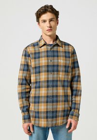 Flanellskjorta i brunt, marinblått och vitt rutmönster. Har en knäppbar krage, långa ärmar och en bröstficka. Texturerad tyg.