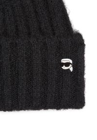 Zwarte gebreide beanie met geribbelde textuur en een kleine, witte speld met daarop een figuur die een zonnebril draagt. Zacht materiaal en casual ontwerp.