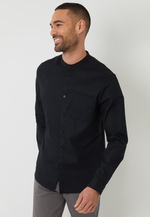 Camisa negra de botones con cuello mao, bolsillo frontal y mangas largas; hecha de una tela suave con una textura sólida.