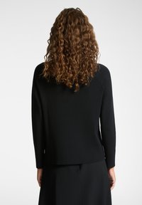 Svart ribbad tröja med långa ärmar, rund hals och avslappnad passform. Texturen är jämn med ett subtilt horisontellt mönster som är synligt.