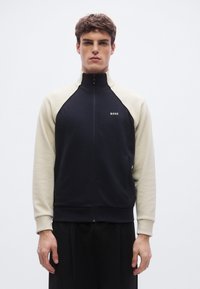 Laivastonsininen ja kerma värinen vetoketjullinen collegepaita korkealla kauluksella, raglan-hihoilla, sivutaskuilla ja pienellä logolla rinnassa. Pehmeä pinta.