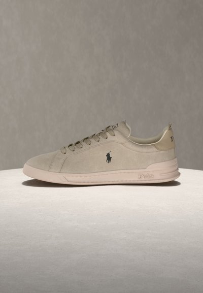 Μπέζ αθλητικό παπούτσι χαμηλής κοπής με κορδόνια, λογότυπο Polo στο πλάι και το «Polo» ανάγλυφο στη λαστιχένια σόλα, εκτεθειμένο σε φωτεινή επιφάνεια.