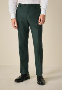 Dark green, textured tailored trousers with a straight cut, featuring a front crease and a single button closure. Worn with black dress shoes.