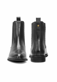 Czarne skórzane botki za kostkę pokazane z przodu i z tyłu, z uchwytami do zakupu i niskimi, zabudowanymi obcasami.