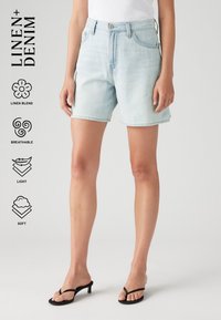 Lichtblauwe linnenmix denim short met een mid-rise taille, standaardzakken en een zachte, ademende textuur. Gecombineerd met zwarte sandalen.