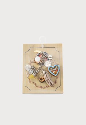 Pulsera con cadena de plata, charm de pretzel falso, charm en forma de corazón con el texto "O'zapft is!", cuerno amarillo y borla beige sobre tarjeta decorativa beige.