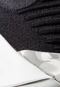 Sorte strikkede sneakers med en strukturert, teksturert overdel og en mønstret grå og hvit hælakkent; har en glatt hvit såle.