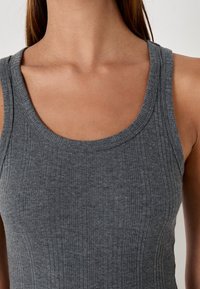 Camiseta de tirantes gris con un escote redondo y tirantes anchos. La textura es suave, con acanalados verticales en toda la prenda.