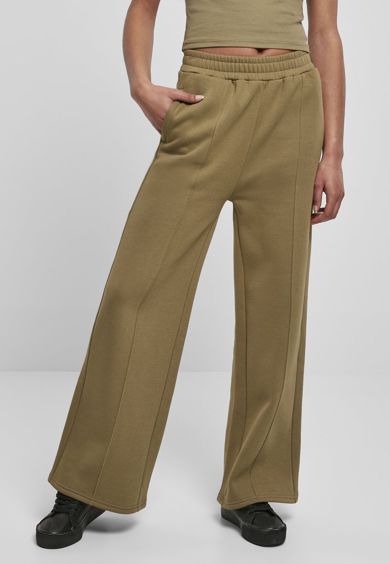 Khakifarbene weite Hose aus weichem, dehnbarem Material mit elastischem Bund, seitlichen Taschen und vertikalen Nähten für zusätzliche Details.