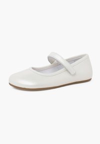 Zapato Mary Jane de cuero blanco y brillante con punta redonda y una correa de velcro. Suela plana con una ligera textura, adecuada para un uso casual.