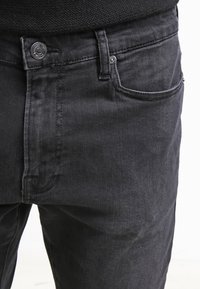 Mustad jeanid, slim fit, esikülje tasku, nupuga kinnitamine ja õrnad õmblusestikud. Sile tekstuur, minimaalsed kaunistused.