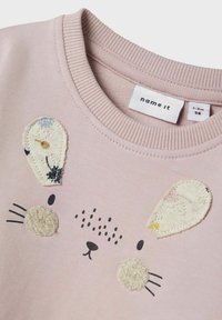 Felpa rosa con un design di coniglio, dotata di orecchie ricamate, naso testurizzato e dettagli facciali neri cuciti. Collo a costine.