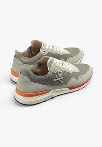 Graue und beige Sneakers mit einem Totenkopf-Logo, strukturiertem Stoff, weißen Schnürsenkeln und orangefarbenen Akzenten auf der Sohle, mit einem abgerundeten Zehendesign.