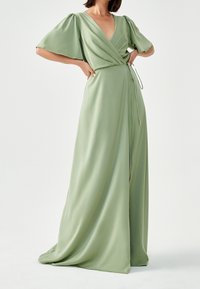 Lång, flödande omslagsklänning i ljusgrön satin med korta puffärmar, V-ringning och justerbar knytning i midjan. Mjukt material, minimala detaljer.