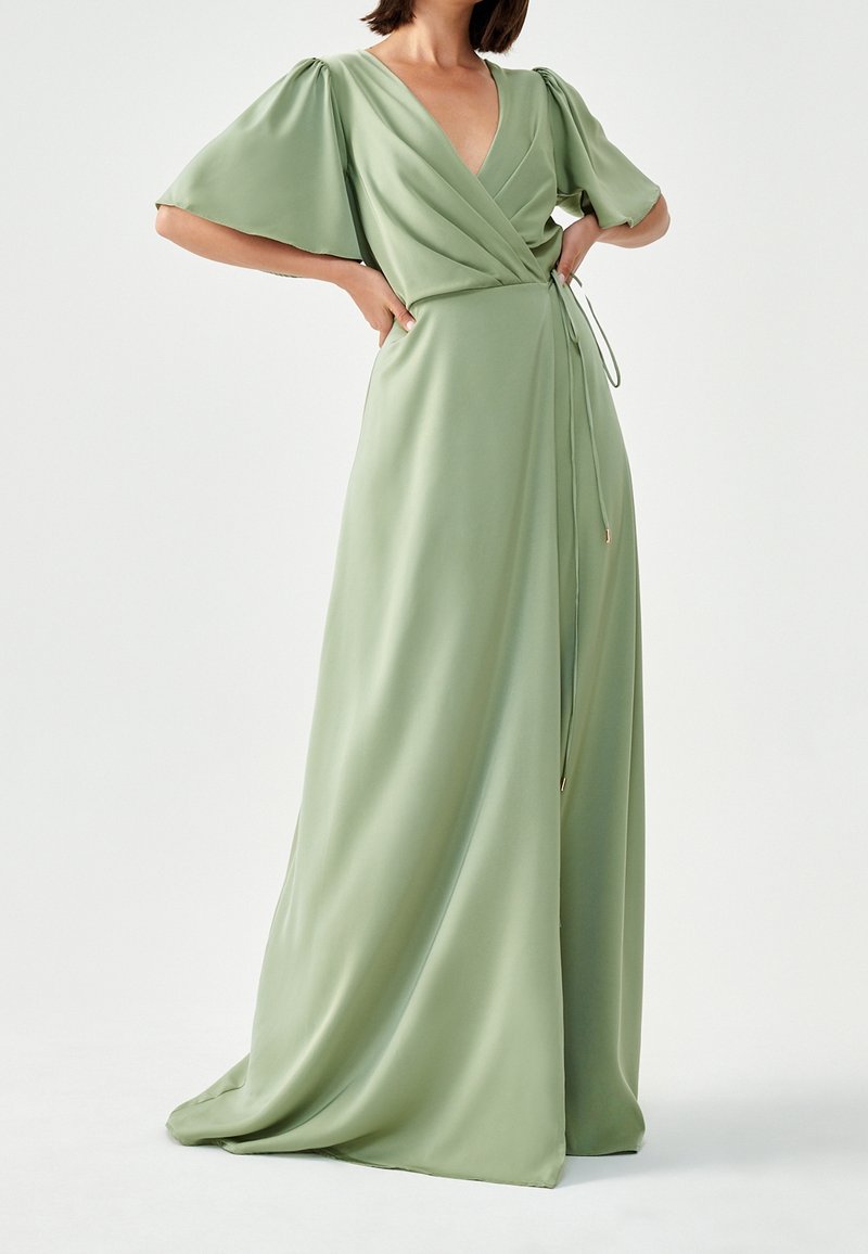 Lång, flödande omslagsklänning i ljusgrön satin med korta puffärmar, V-ringning och justerbar knytning i midjan. Mjukt material, minimala detaljer.